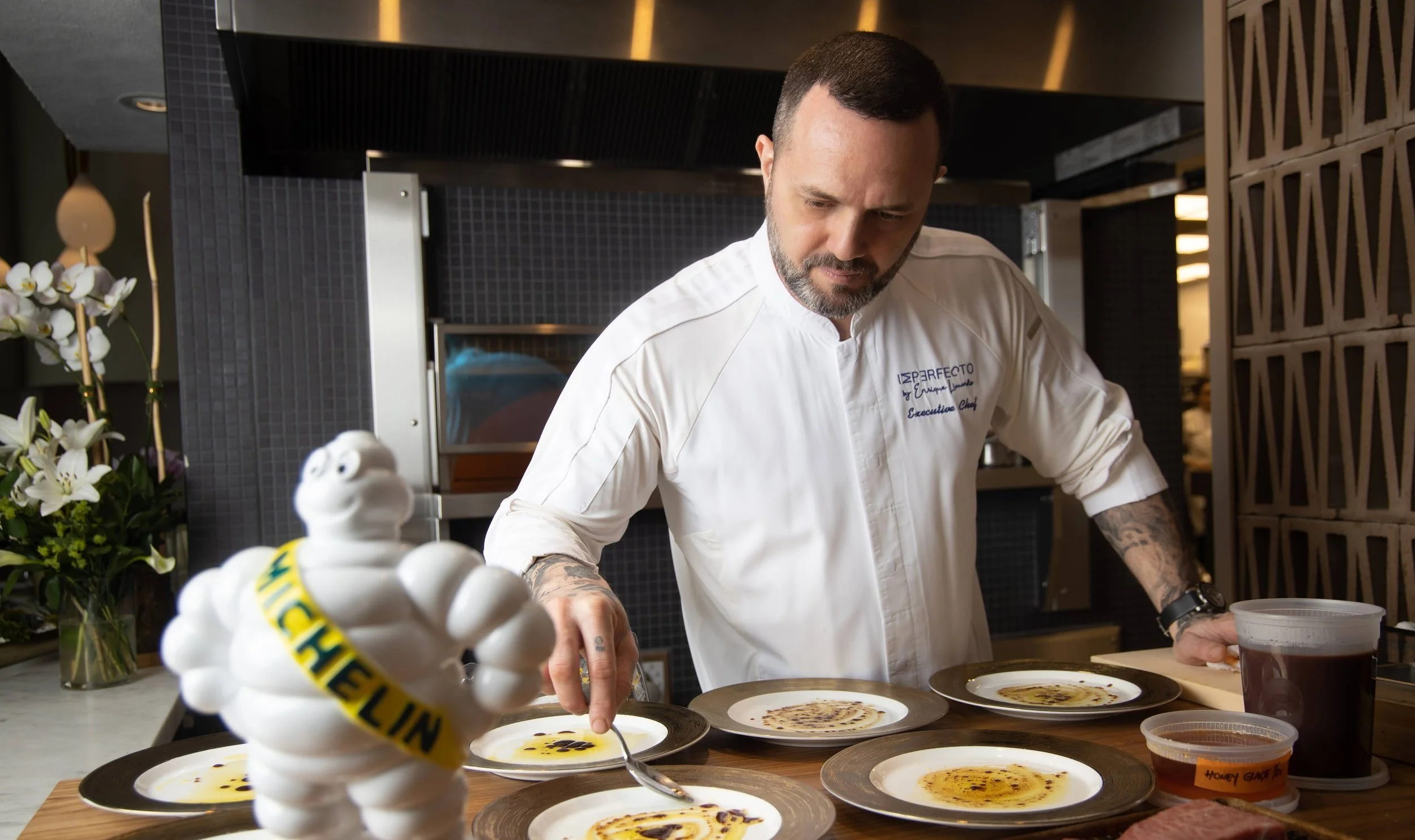 Chef Enrique Limardo plating a course in the kitchen at Imperfecto, beside a Michelin figure