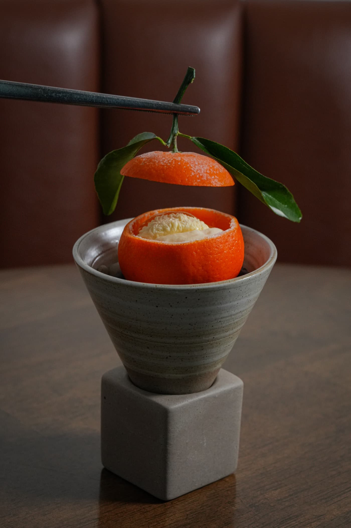 A mandarin becomes something unexpected: tweezers lift its lid to reveal a filled citrus shell, from Chef Limardo's restaurant work.