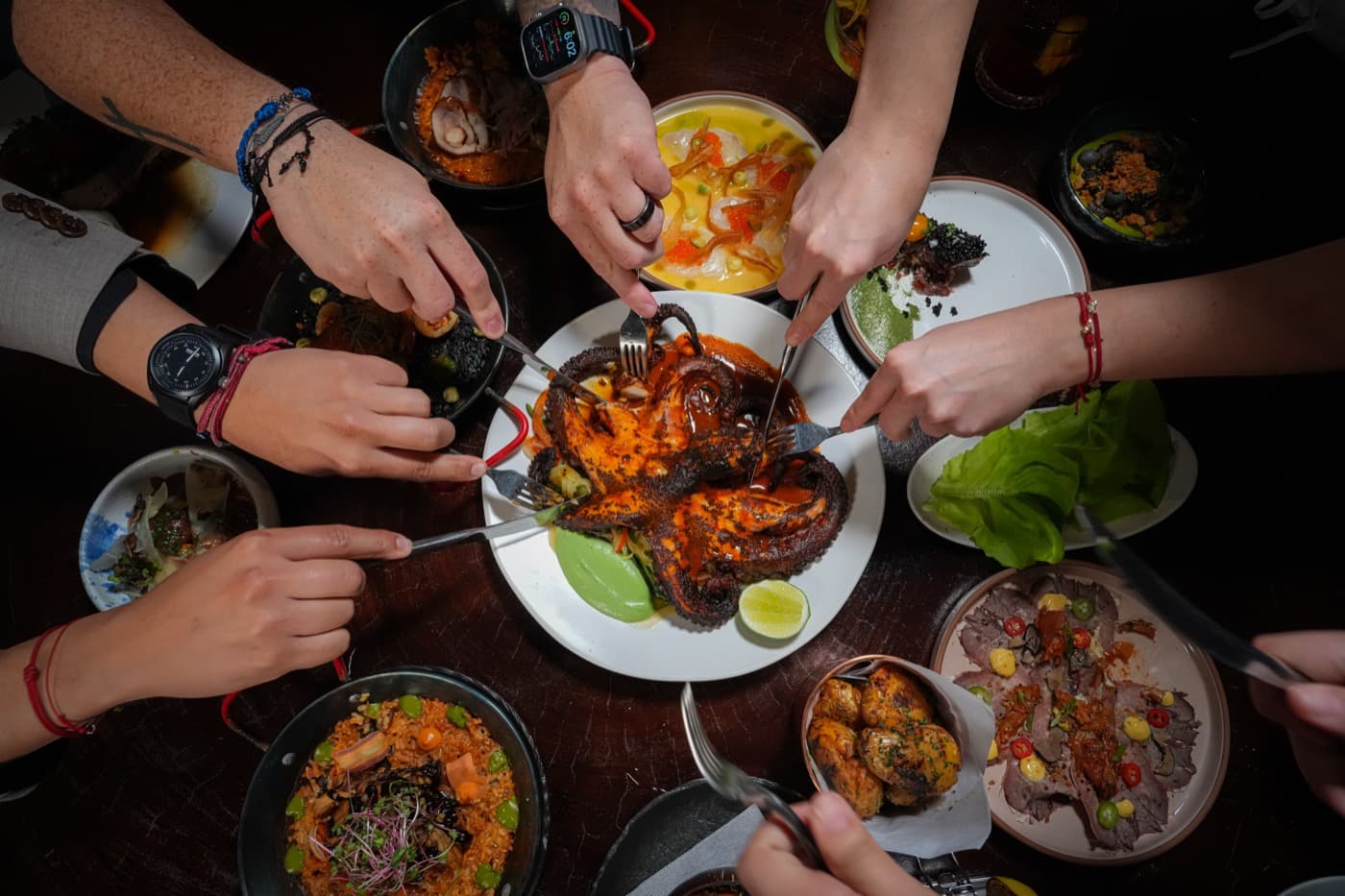 Many hands reaching across a shared table of dishes, seen from above