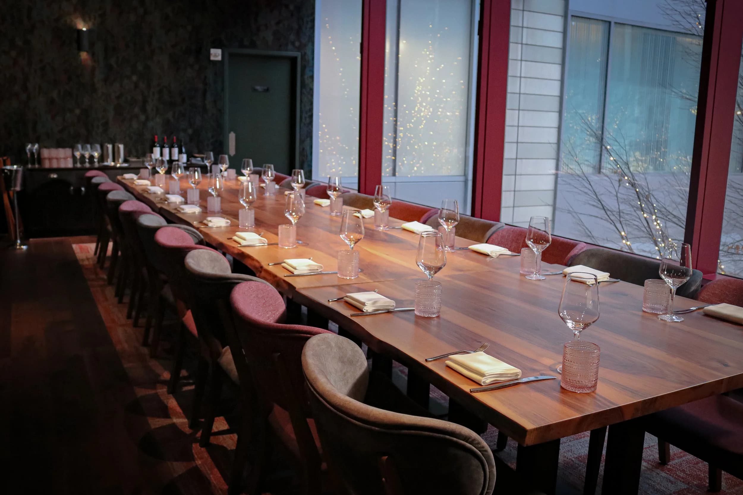 A long wooden table set for a private dinner, lit warmly against evening windows